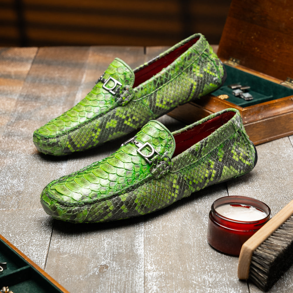 A pair of Marco Di Milano’s Pia Lemon Green driver shoes—crafted from green python skin with black soles and silver buckles—one upright and the other leaning gracefully, showcases the exquisite luxury of handcrafted men’s exotic footwear.