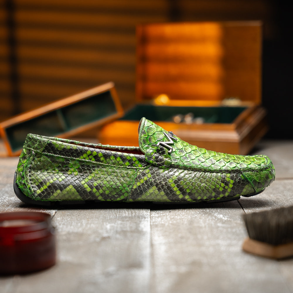 A pair of Marco Di Milano’s Pia Lemon Green driver shoes—crafted from green python skin with black soles and silver buckles—one upright and the other leaning gracefully, showcases the exquisite luxury of handcrafted men’s exotic footwear.
