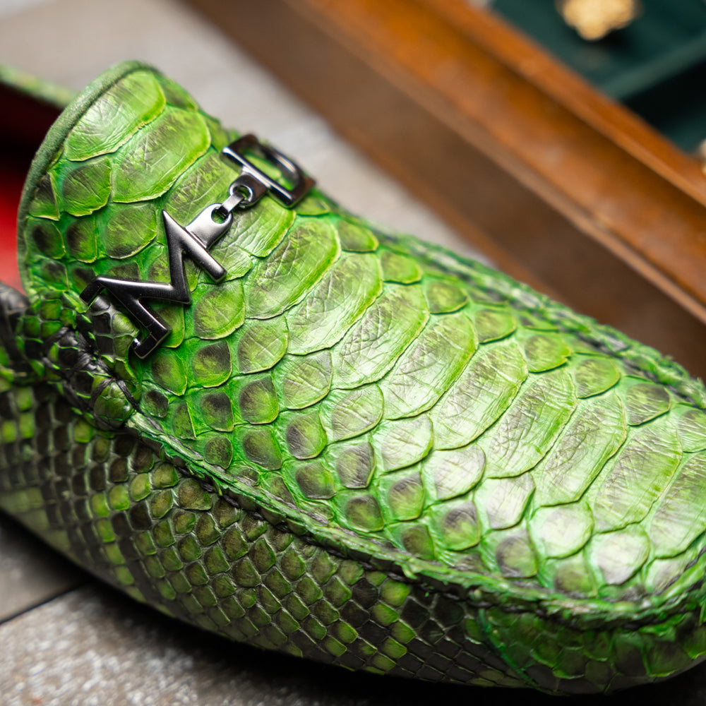 A pair of Marco Di Milano’s Pia Lemon Green driver shoes—crafted from green python skin with black soles and silver buckles—one upright and the other leaning gracefully, showcases the exquisite luxury of handcrafted men’s exotic footwear.