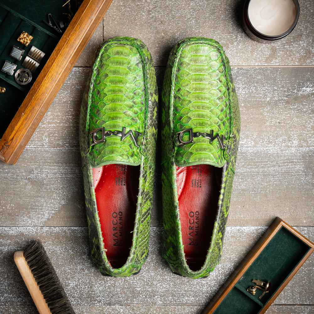 A pair of Marco Di Milano’s Pia Lemon Green driver shoes—crafted from green python skin with black soles and silver buckles—one upright and the other leaning gracefully, showcases the exquisite luxury of handcrafted men’s exotic footwear.