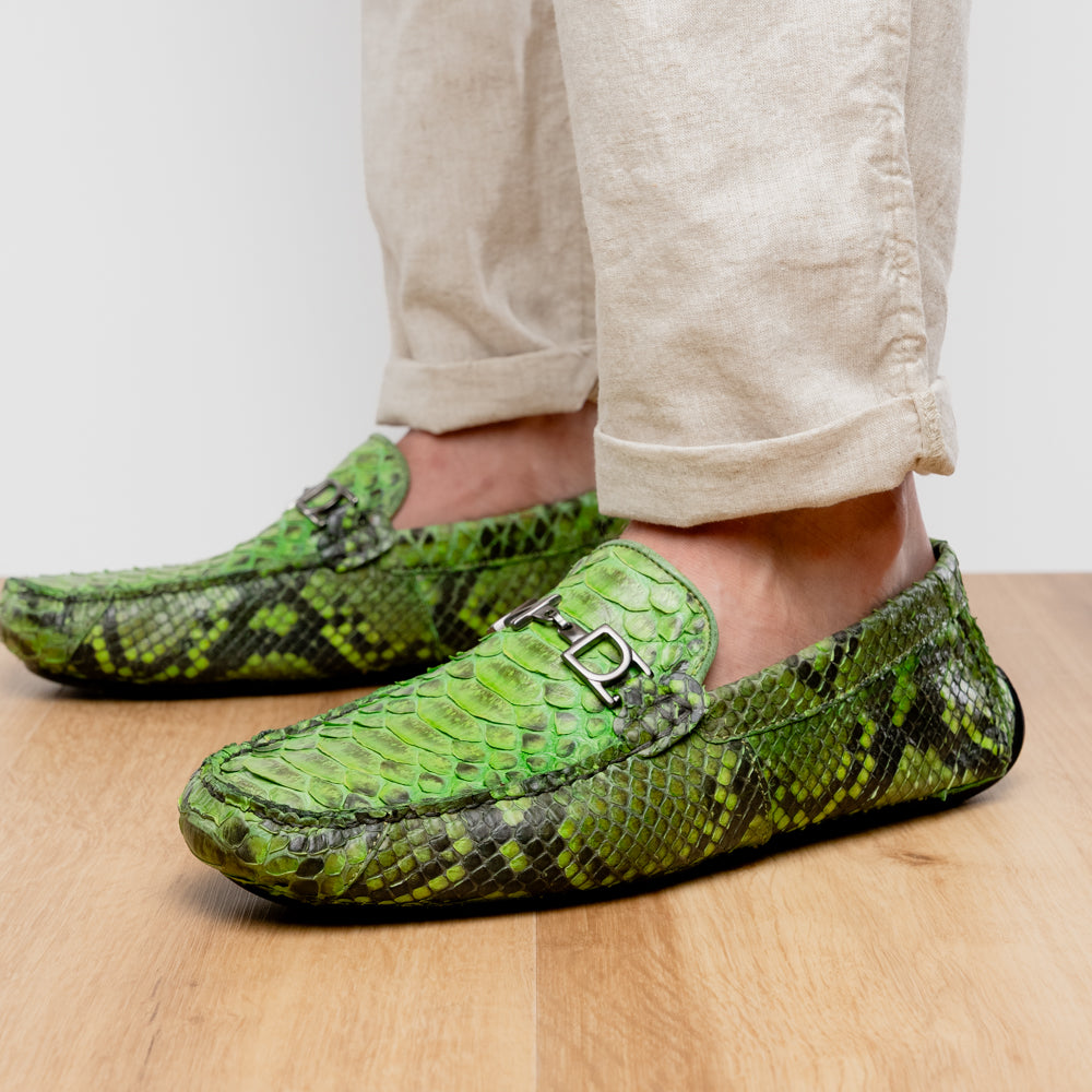 A pair of Marco Di Milano’s Pia Lemon Green driver shoes—crafted from green python skin with black soles and silver buckles—one upright and the other leaning gracefully, showcases the exquisite luxury of handcrafted men’s exotic footwear.