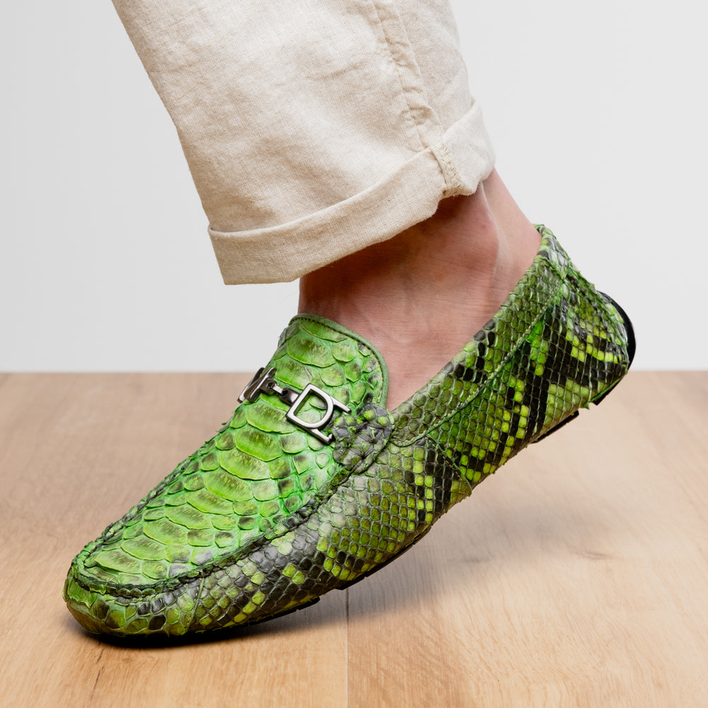 A pair of Marco Di Milano’s Pia Lemon Green driver shoes—crafted from green python skin with black soles and silver buckles—one upright and the other leaning gracefully, showcases the exquisite luxury of handcrafted men’s exotic footwear.