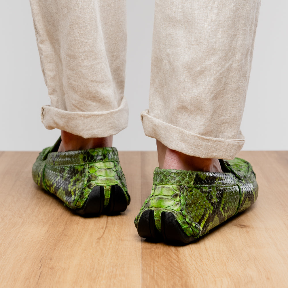 A pair of Marco Di Milano’s Pia Lemon Green driver shoes—crafted from green python skin with black soles and silver buckles—one upright and the other leaning gracefully, showcases the exquisite luxury of handcrafted men’s exotic footwear.