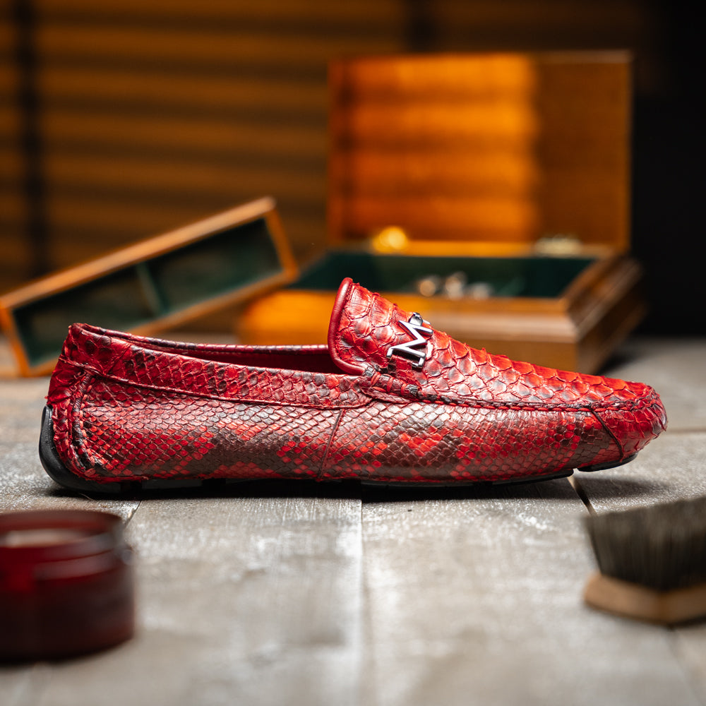 A pair of Pia Red loafers by Marco Di Milano—crafted as luxury men’s driver shoes in a striking red snakeskin pattern, featuring black rubber soles and silver buckle detailing, with one shoe upright and the other displayed on its side—showcase the allure of exotic python-inspired style in a distinguished design.