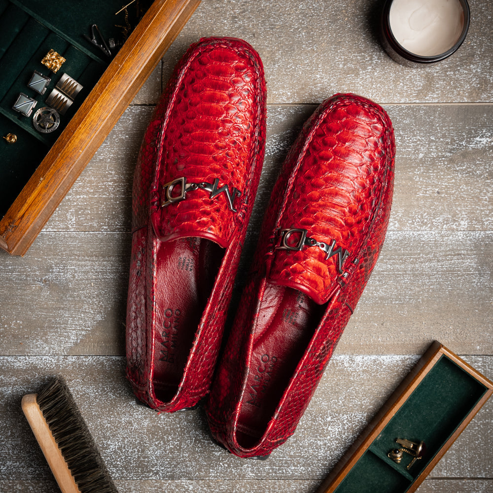 A pair of Pia Red loafers by Marco Di Milano—crafted as luxury men’s driver shoes in a striking red snakeskin pattern, featuring black rubber soles and silver buckle detailing, with one shoe upright and the other displayed on its side—showcase the allure of exotic python-inspired style in a distinguished design.