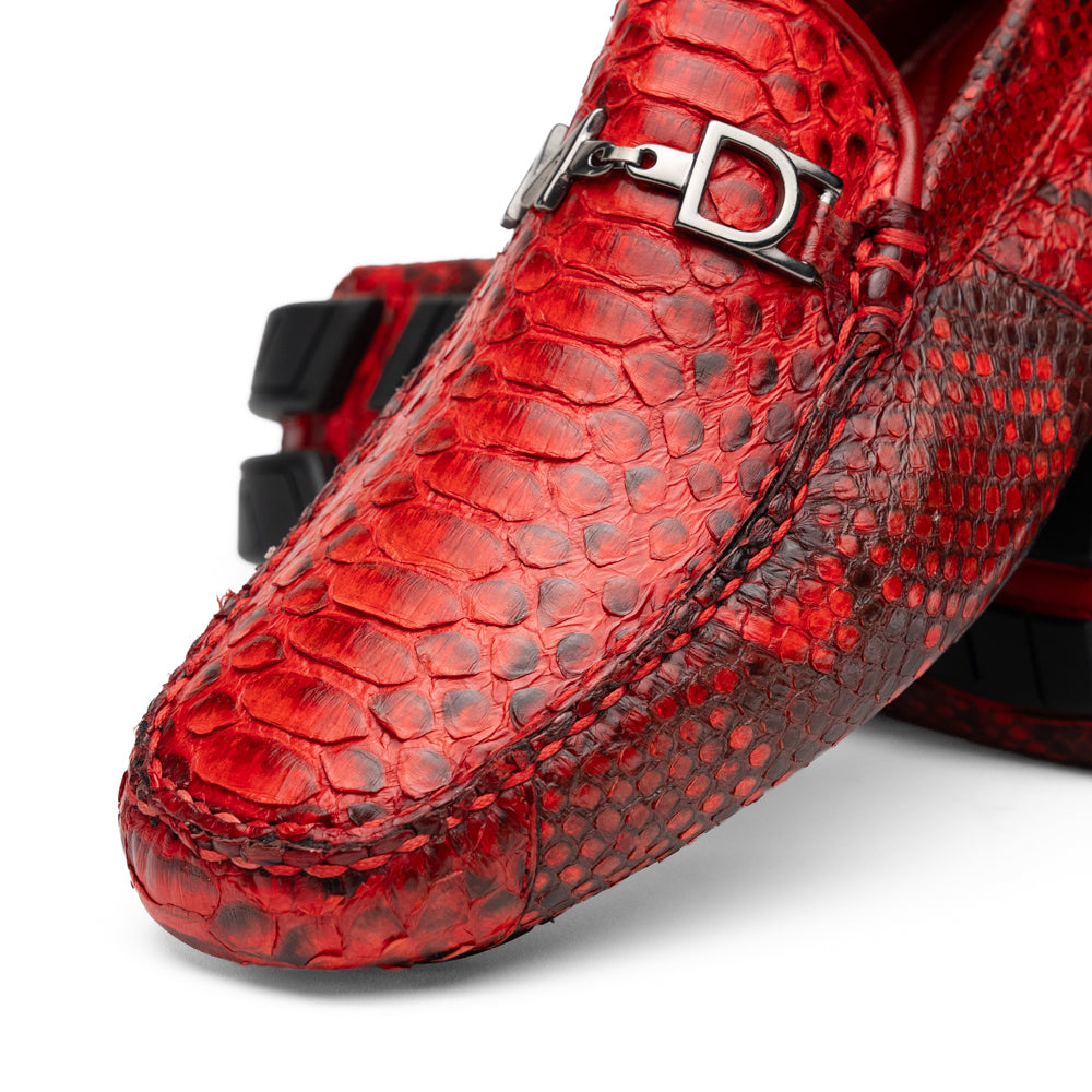A pair of Pia Red loafers by Marco Di Milano—crafted as luxury men’s driver shoes in a striking red snakeskin pattern, featuring black rubber soles and silver buckle detailing, with one shoe upright and the other displayed on its side—showcase the allure of exotic python-inspired style in a distinguished design.