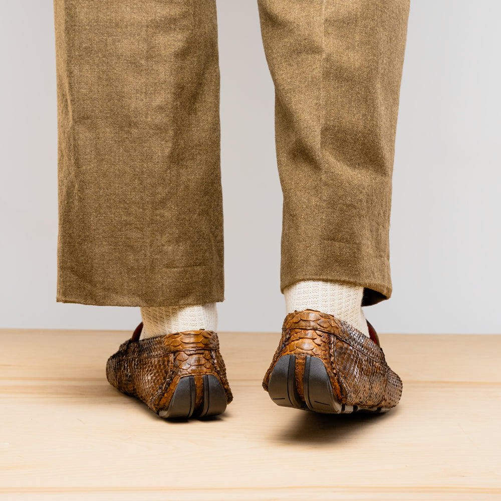 The Marco Di Milano Pia Cognac features brown python skin driver loafers with a metal buckle, visible black rubber soles, and one shoe upright while the other lies flat—a luxury men's shoe designed for style seekers.