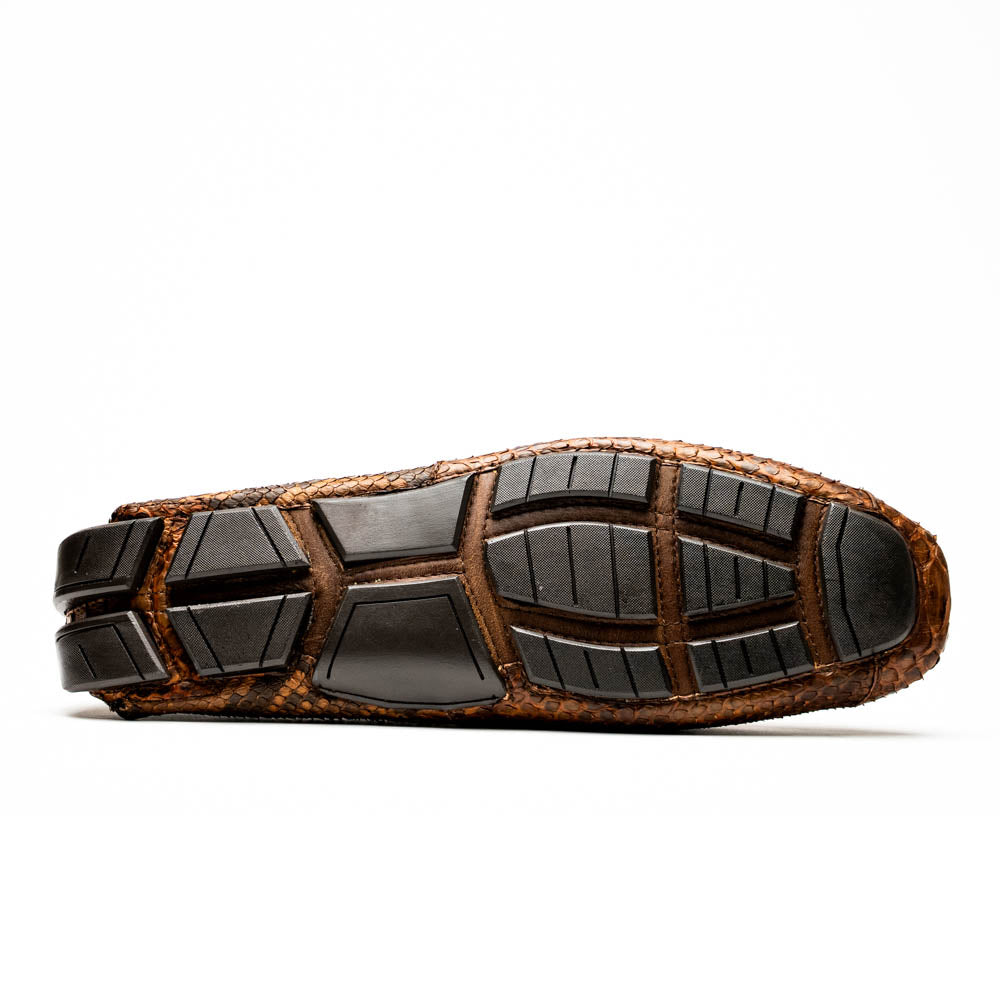 The Marco Di Milano Pia Cognac features brown python skin driver loafers with a metal buckle, visible black rubber soles, and one shoe upright while the other lies flat—a luxury men's shoe designed for style seekers.