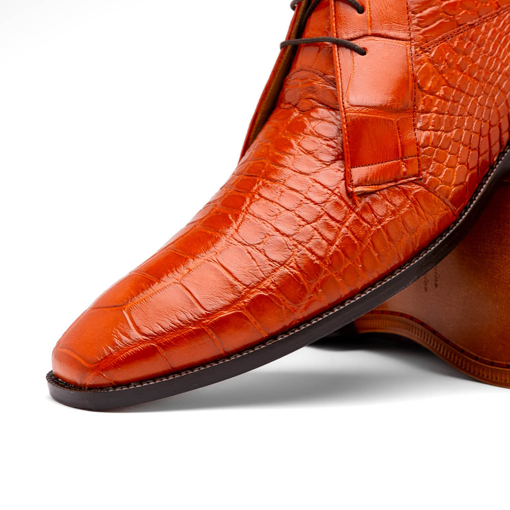 The Pietro Honey boots by Marco Di Milano are orange-brown genuine alligator, hand-painted with crocodile texture—displayed upright and sideway to show the sole—ideal for luxury footwear enthusiasts.