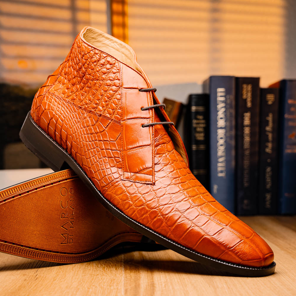 The Pietro Honey boots by Marco Di Milano are orange-brown genuine alligator, hand-painted with crocodile texture—displayed upright and sideway to show the sole—ideal for luxury footwear enthusiasts.