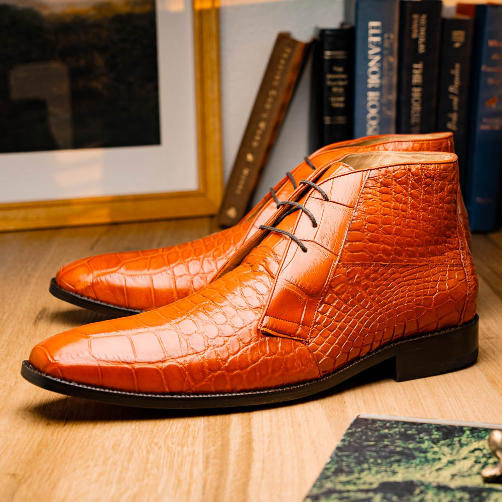 The Pietro Honey boots by Marco Di Milano are orange-brown genuine alligator, hand-painted with crocodile texture—displayed upright and sideway to show the sole—ideal for luxury footwear enthusiasts.