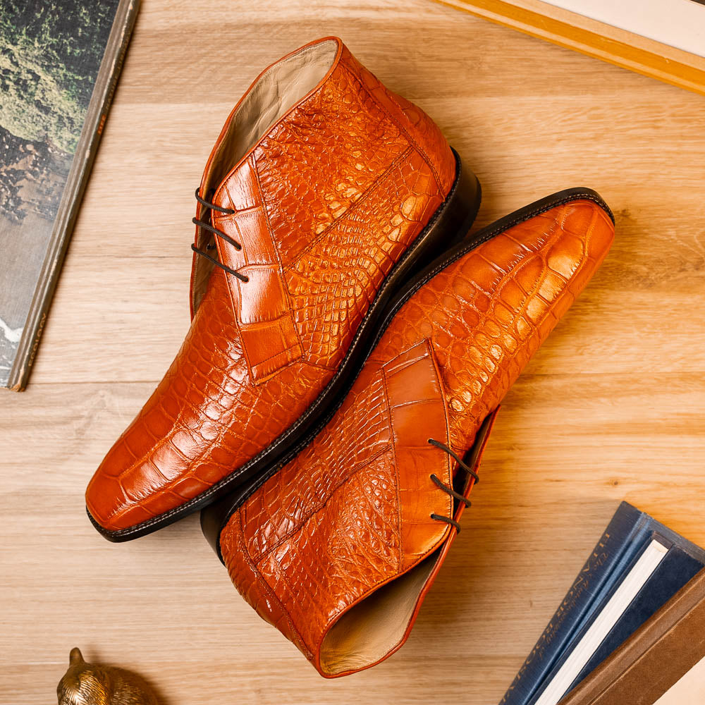 The Pietro Honey boots by Marco Di Milano are orange-brown genuine alligator, hand-painted with crocodile texture—displayed upright and sideway to show the sole—ideal for luxury footwear enthusiasts.