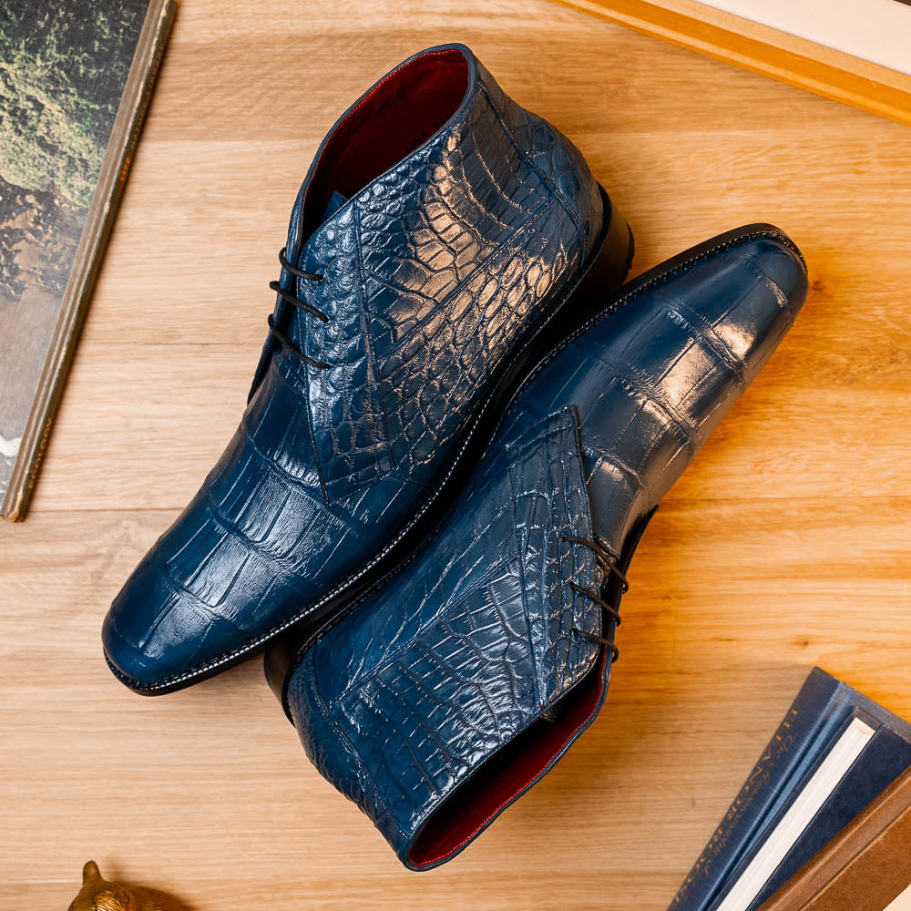 The Marco Di Milano "Pietro Blue Jeans" are luxury men's lace-up boots in blue crocodile-pattern leather, with one standing upright and the other tilted to reveal the tan embossed sole.