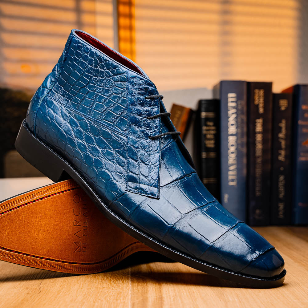 The Marco Di Milano "Pietro Blue Jeans" are luxury men's lace-up boots in blue crocodile-pattern leather, with one standing upright and the other tilted to reveal the tan embossed sole.
