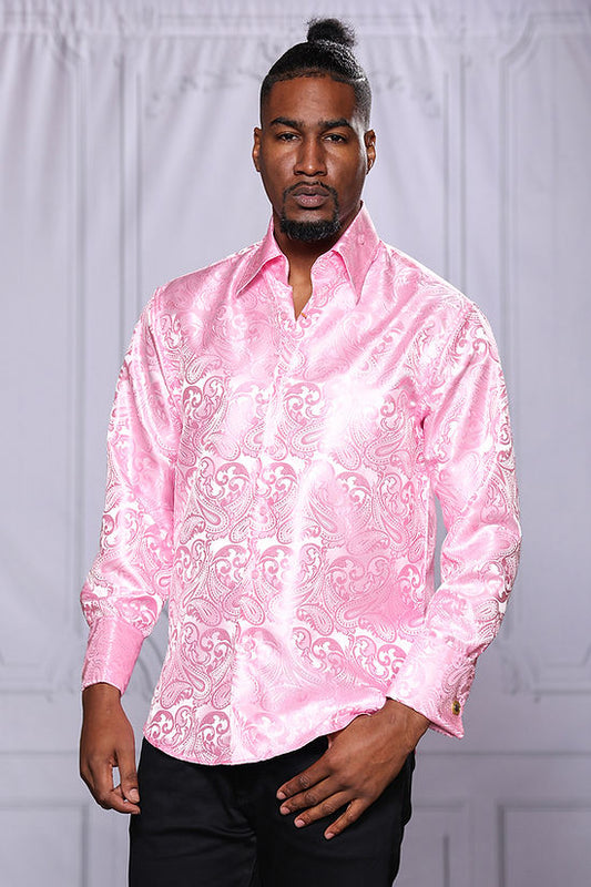 A man stands indoors facing the camera, wearing the Manzini MANZINI MZT-100 Paisley Long Sleeve Satin Pink Shirt w/ Links and black pants—an eye-catching look from Manzini, perfect for formal events.