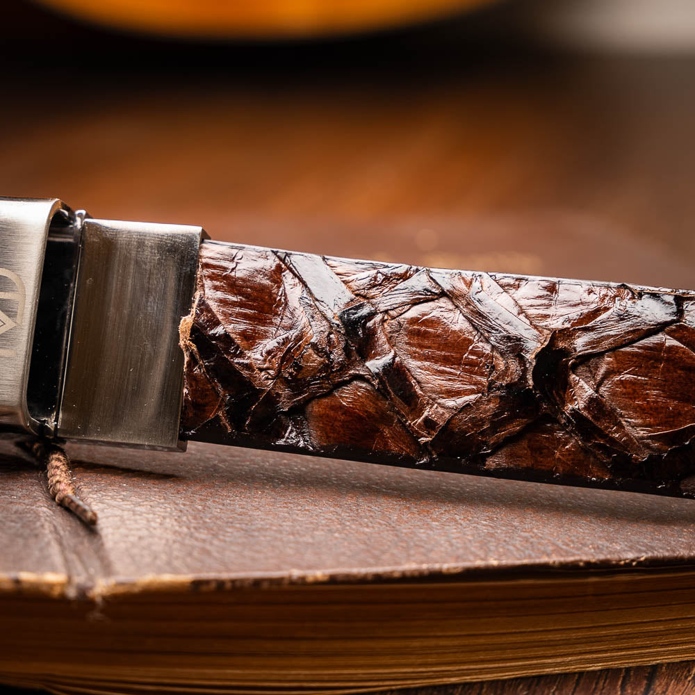 The Olivieri Belt Brown by Marco Di Milano is a genuine pirarucu leather belt with a textured finish, silver buckle, and "MD" initials—ideal for pairing with luxury footwear.