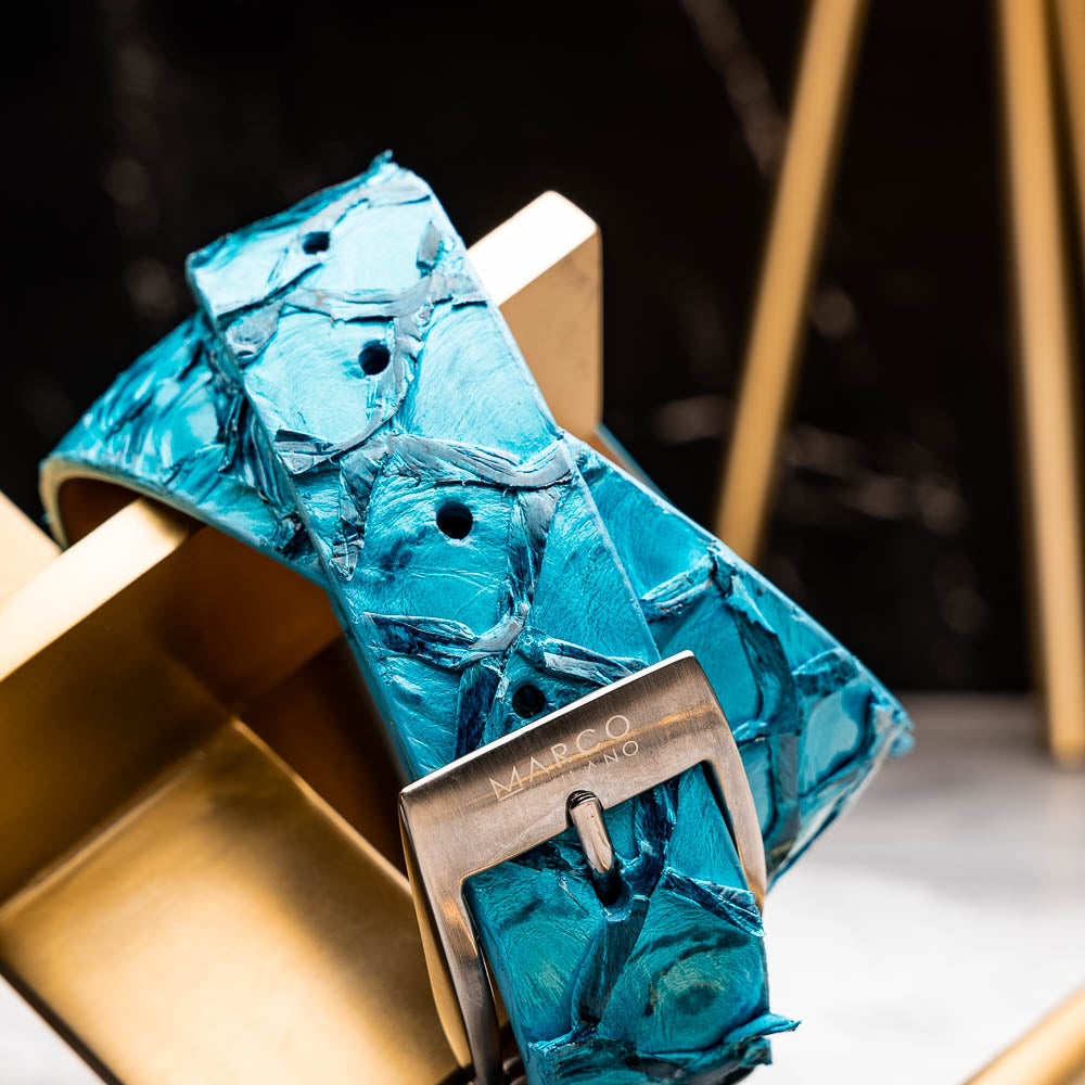 The Olivieri Belt Caribbean Blue by Marco Di Milano, made from genuine pirarucu with a textured turquoise finish and a silver logo buckle, is shown coiled on a white background.