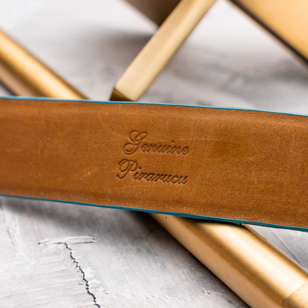 The Olivieri Belt Caribbean Blue by Marco Di Milano, made from genuine pirarucu with a textured turquoise finish and a silver logo buckle, is shown coiled on a white background.