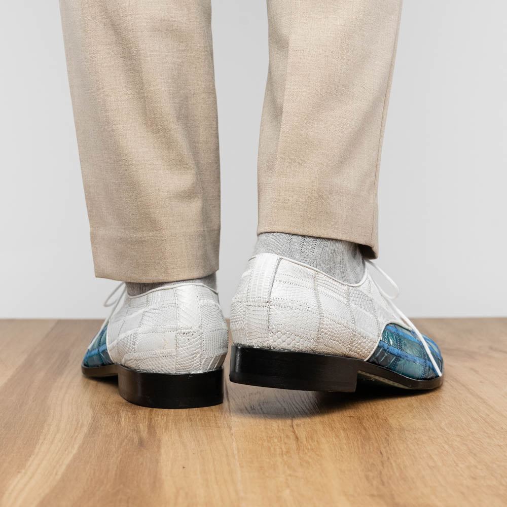 The "Pissa Aqua/White" by Marco Di Milano is a men's dress shoe with a white textured upper, teal blue patterned lower, hand-painted finishes, white laces, and a black sole—showcasing luxury style and craftsmanship.