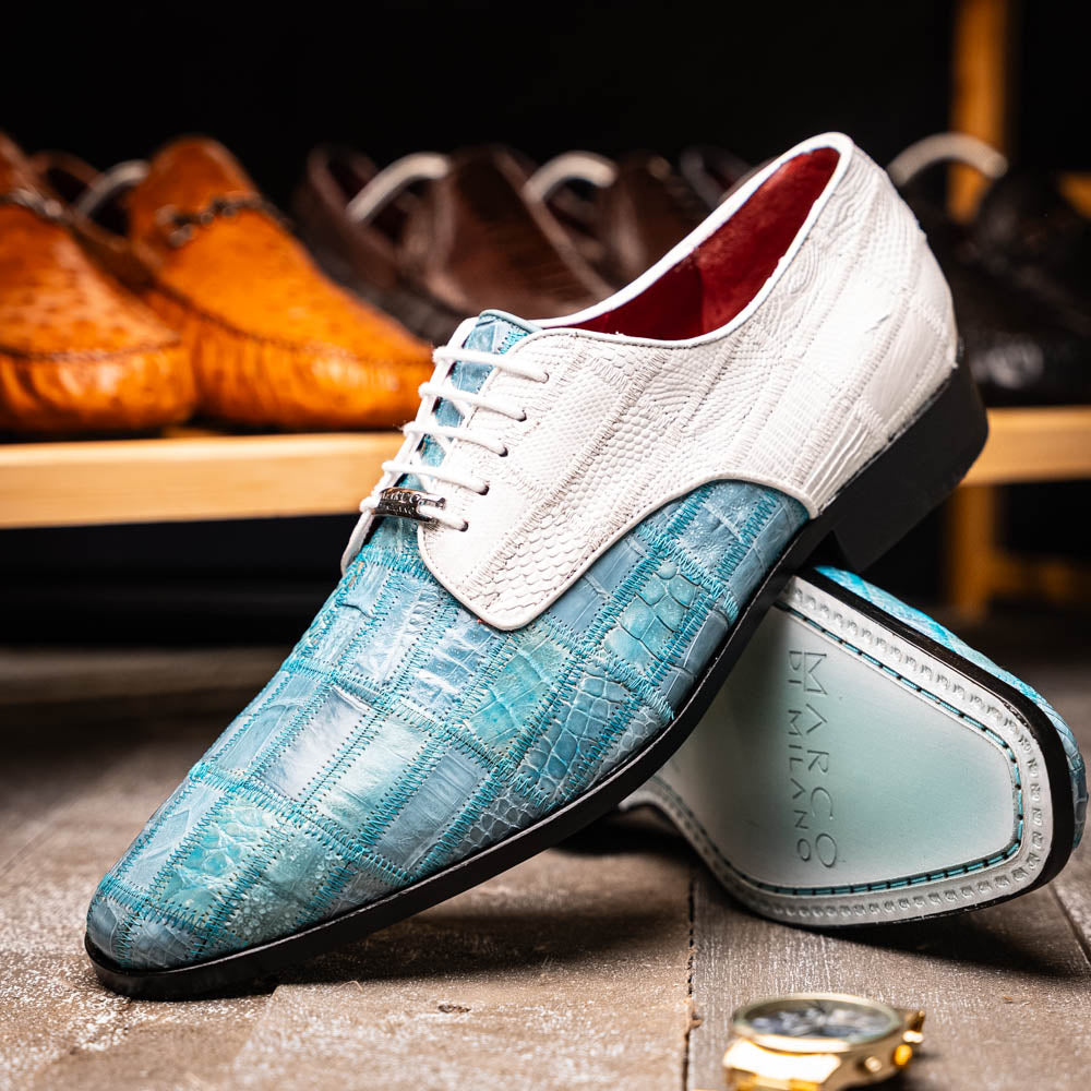 The "Pissa Aqua/White" by Marco Di Milano is a men's dress shoe with a white textured upper, teal blue patterned lower, hand-painted finishes, white laces, and a black sole—showcasing luxury style and craftsmanship.