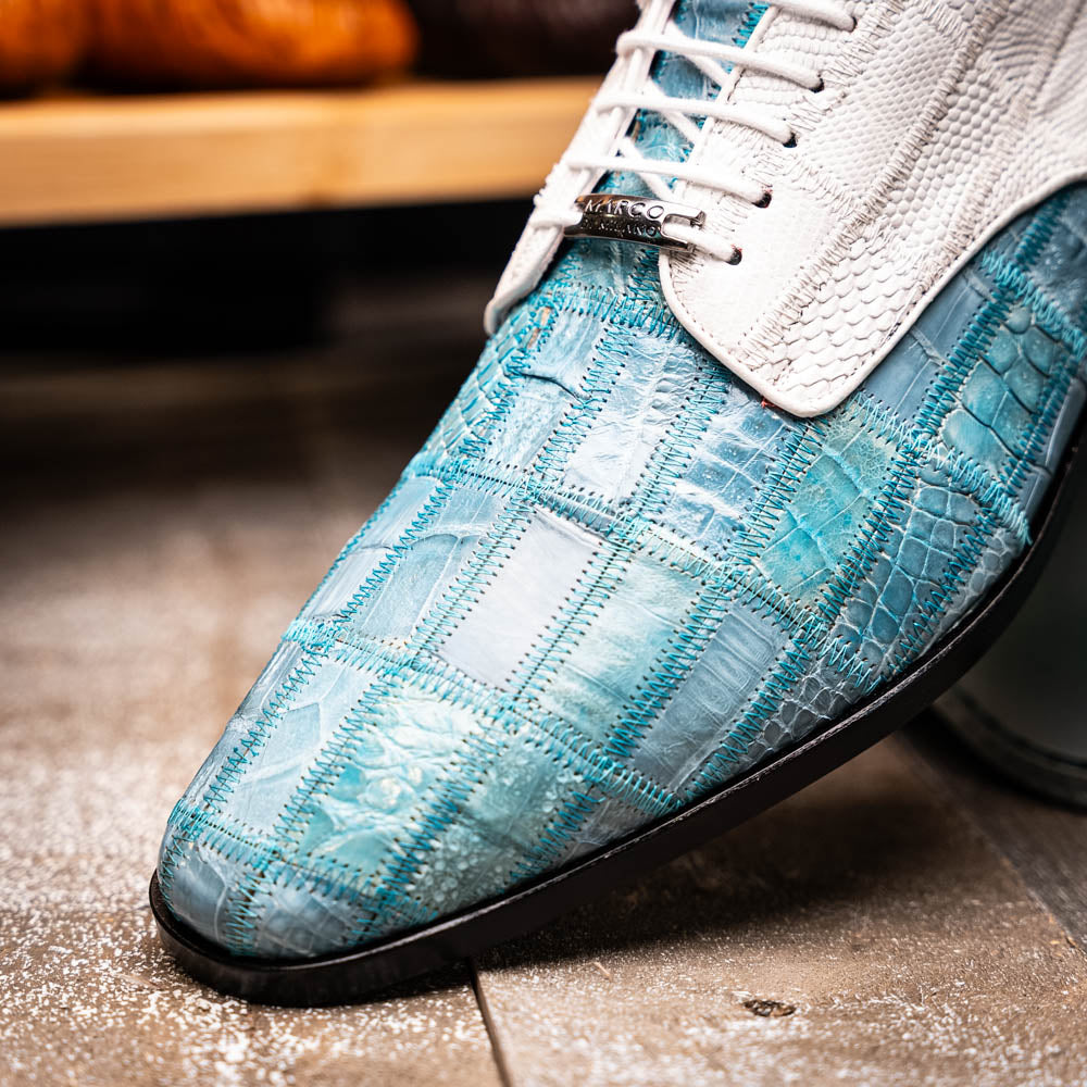 The "Pissa Aqua/White" by Marco Di Milano is a men's dress shoe with a white textured upper, teal blue patterned lower, hand-painted finishes, white laces, and a black sole—showcasing luxury style and craftsmanship.
