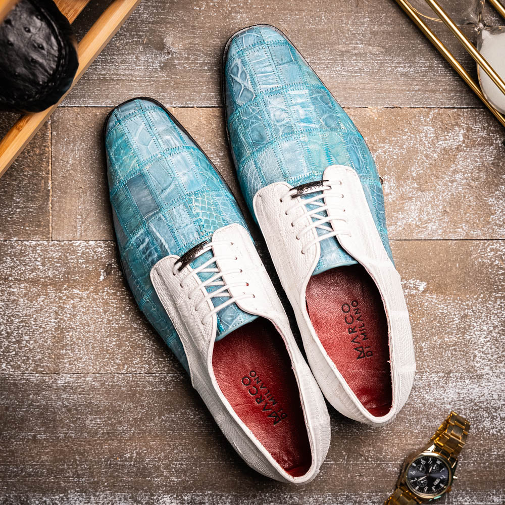 The "Pissa Aqua/White" by Marco Di Milano is a men's dress shoe with a white textured upper, teal blue patterned lower, hand-painted finishes, white laces, and a black sole—showcasing luxury style and craftsmanship.
