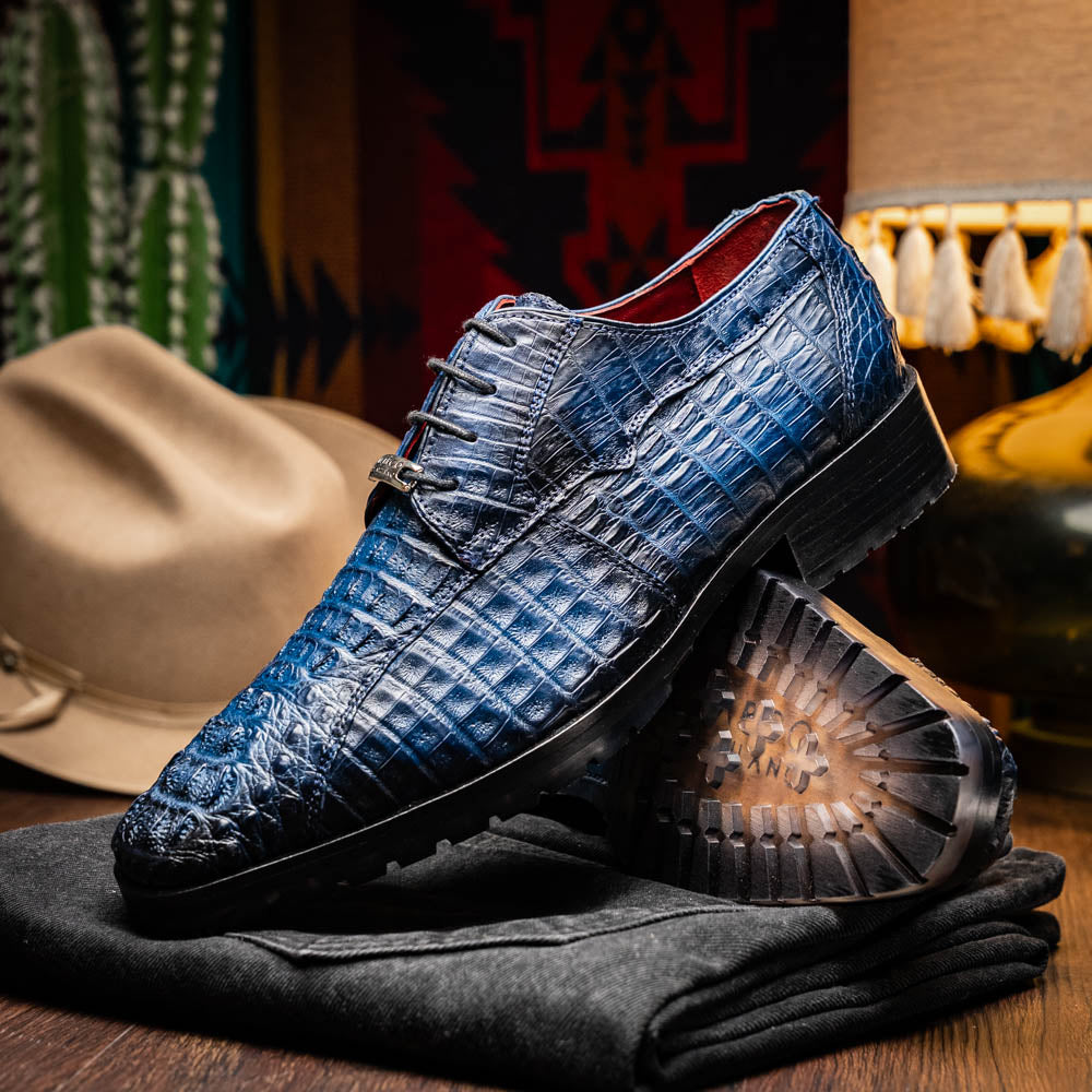 The Marco Di Milano Ragusa Stained Navy is a pair of luxury men's dress shoes in blue crocodile-patterned leather—one upright, one angled to display the sole—handcrafted for sophistication and timeless style.