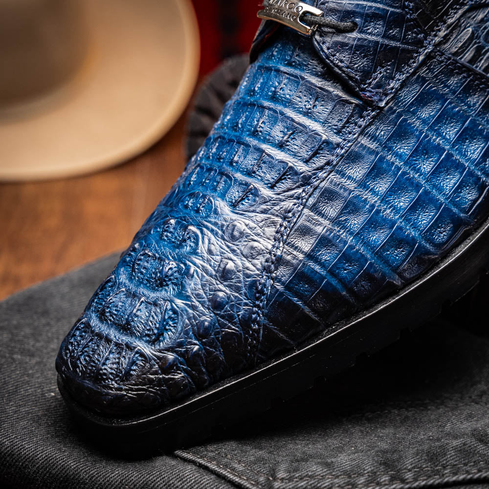 The Marco Di Milano Ragusa Stained Navy is a pair of luxury men's dress shoes in blue crocodile-patterned leather—one upright, one angled to display the sole—handcrafted for sophistication and timeless style.