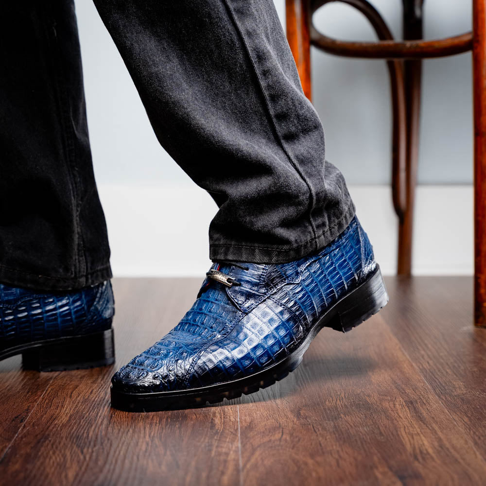The Marco Di Milano Ragusa Stained Navy is a pair of luxury men's dress shoes in blue crocodile-patterned leather—one upright, one angled to display the sole—handcrafted for sophistication and timeless style.