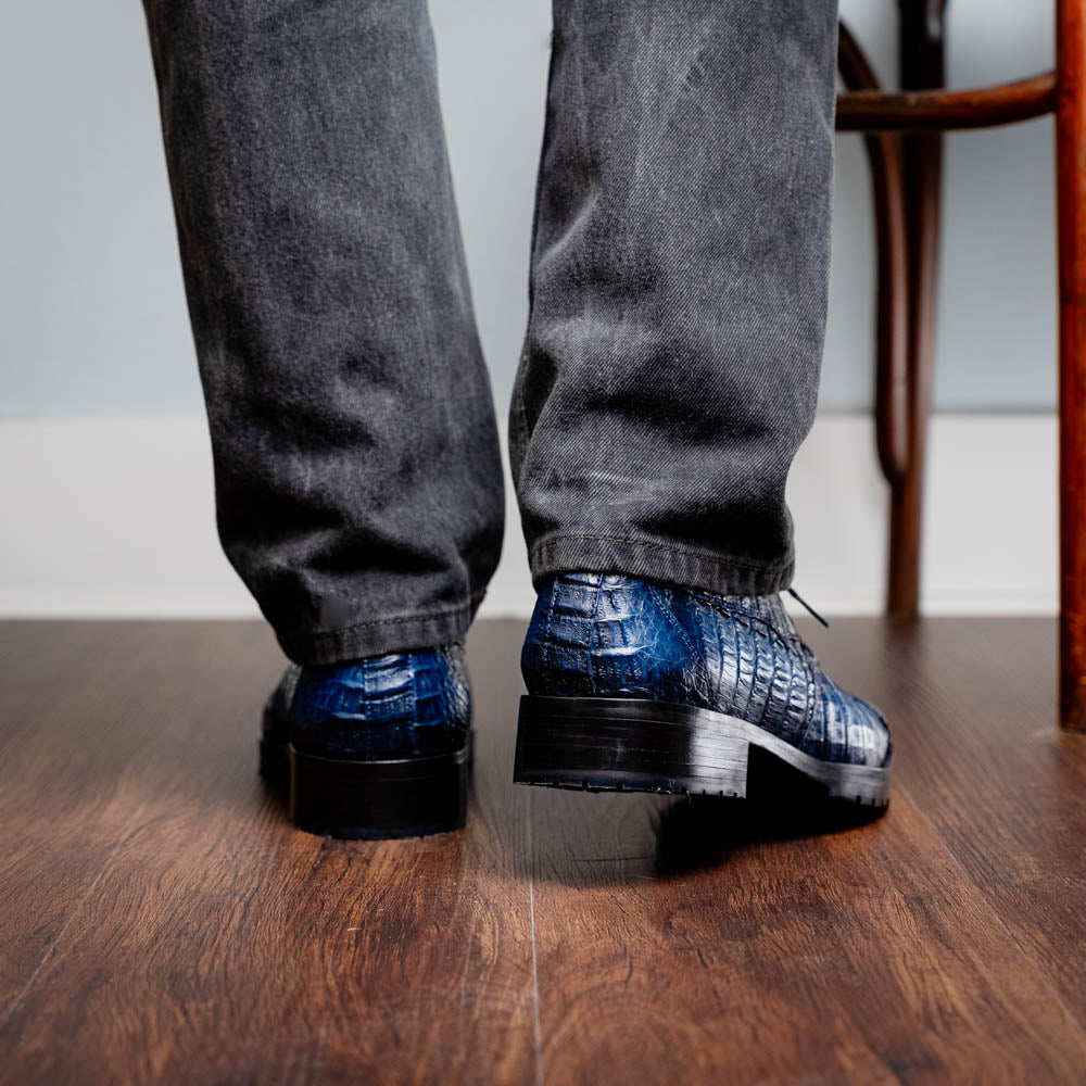 The Marco Di Milano Ragusa Stained Navy is a pair of luxury men's dress shoes in blue crocodile-patterned leather—one upright, one angled to display the sole—handcrafted for sophistication and timeless style.