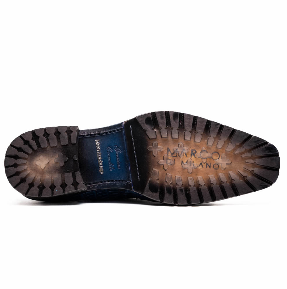 The Marco Di Milano Ragusa Stained Navy is a pair of luxury men's dress shoes in blue crocodile-patterned leather—one upright, one angled to display the sole—handcrafted for sophistication and timeless style.