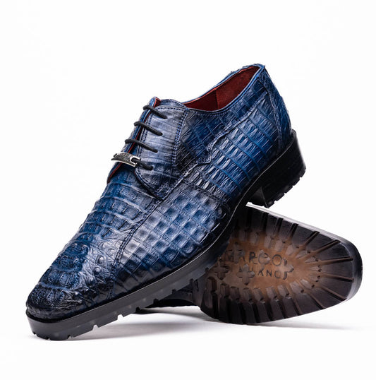 The Marco Di Milano Ragusa Stained Navy is a pair of luxury men's dress shoes in blue crocodile-patterned leather—one upright, one angled to display the sole—handcrafted for sophistication and timeless style.
