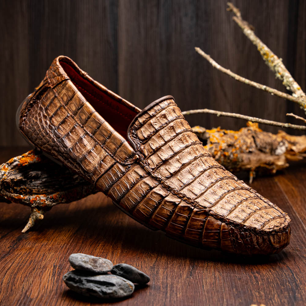 The Remo Washed Brown by Marco Di Milano features luxurious men's loafers with a crocodile texture. One shoe stands upright while the other lies on its side, revealing the detailed sole.