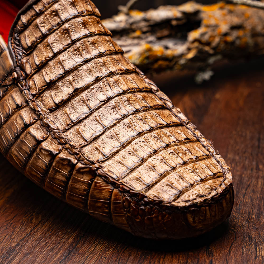 The Remo Washed Brown by Marco Di Milano features luxurious men's loafers with a crocodile texture. One shoe stands upright while the other lies on its side, revealing the detailed sole.