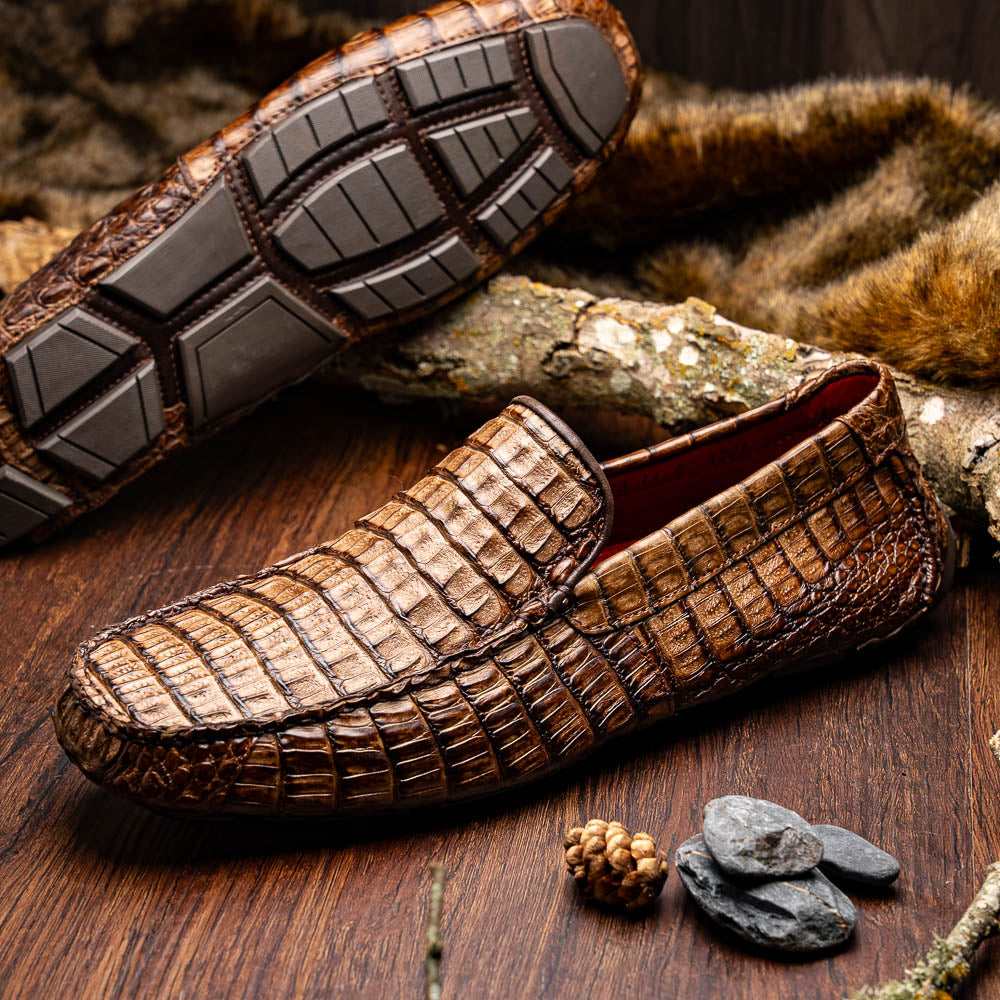 The Remo Washed Brown by Marco Di Milano features luxurious men's loafers with a crocodile texture. One shoe stands upright while the other lies on its side, revealing the detailed sole.