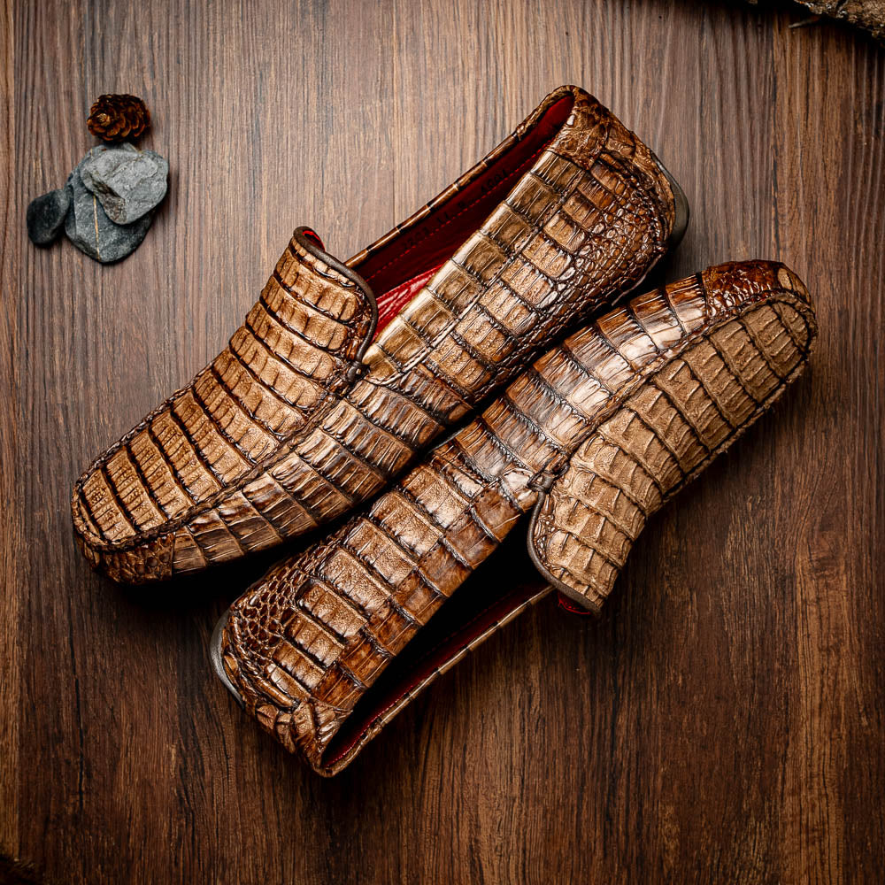 The Remo Washed Brown by Marco Di Milano features luxurious men's loafers with a crocodile texture. One shoe stands upright while the other lies on its side, revealing the detailed sole.