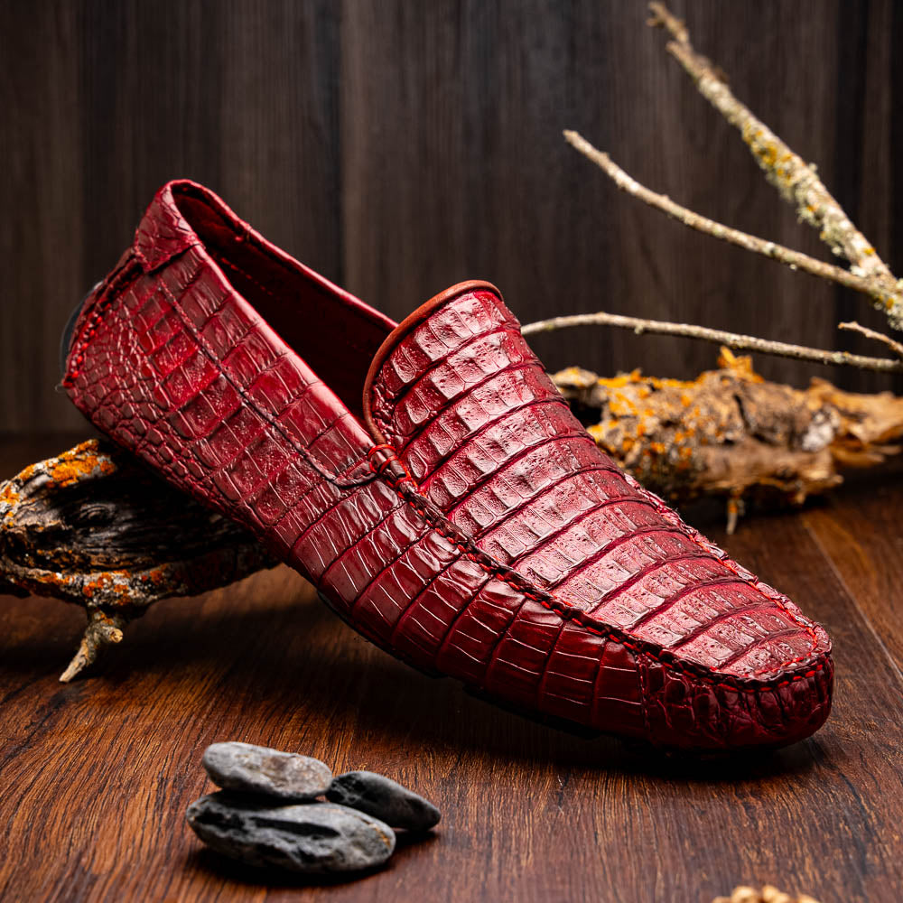 The Marco Di Milano Remo Wine features red crocodile-pattern leather driving shoes: one upright, one on its side showing a black rubber sole with red highlights—ideal for luxury men's footwear enthusiasts.