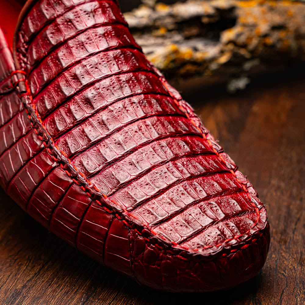 The Marco Di Milano Remo Wine features red crocodile-pattern leather driving shoes: one upright, one on its side showing a black rubber sole with red highlights—ideal for luxury men's footwear enthusiasts.