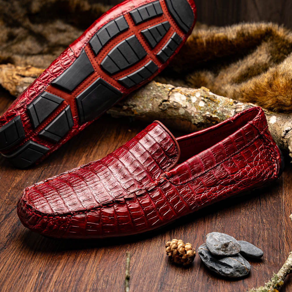 The Marco Di Milano Remo Wine features red crocodile-pattern leather driving shoes: one upright, one on its side showing a black rubber sole with red highlights—ideal for luxury men's footwear enthusiasts.