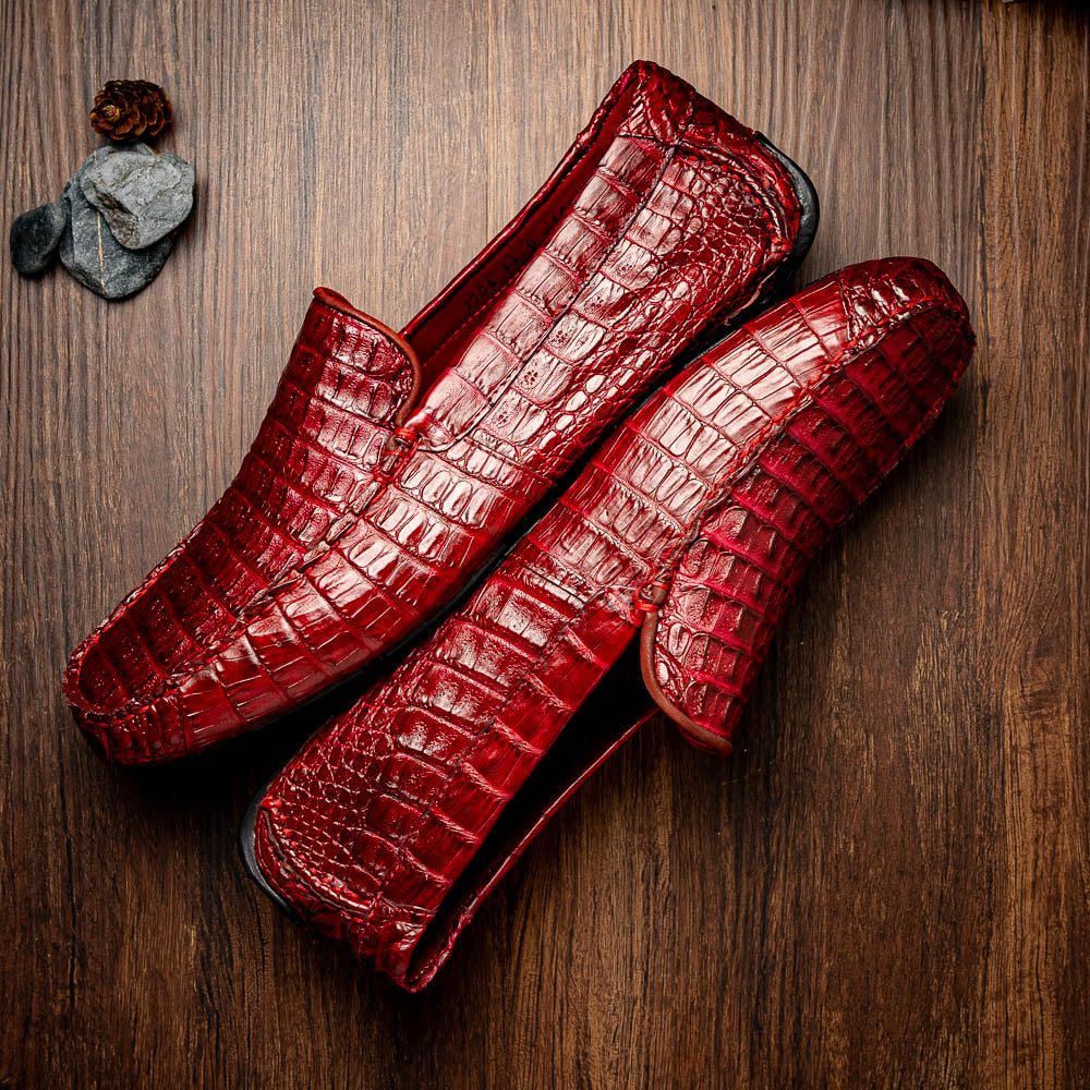 The Marco Di Milano Remo Wine features red crocodile-pattern leather driving shoes: one upright, one on its side showing a black rubber sole with red highlights—ideal for luxury men's footwear enthusiasts.