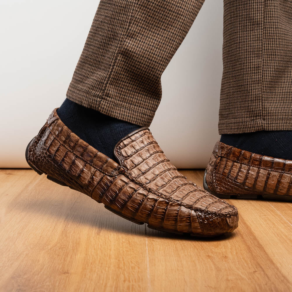 The Remo Washed Brown by Marco Di Milano features luxurious men's loafers with a crocodile texture. One shoe stands upright while the other lies on its side, revealing the detailed sole.