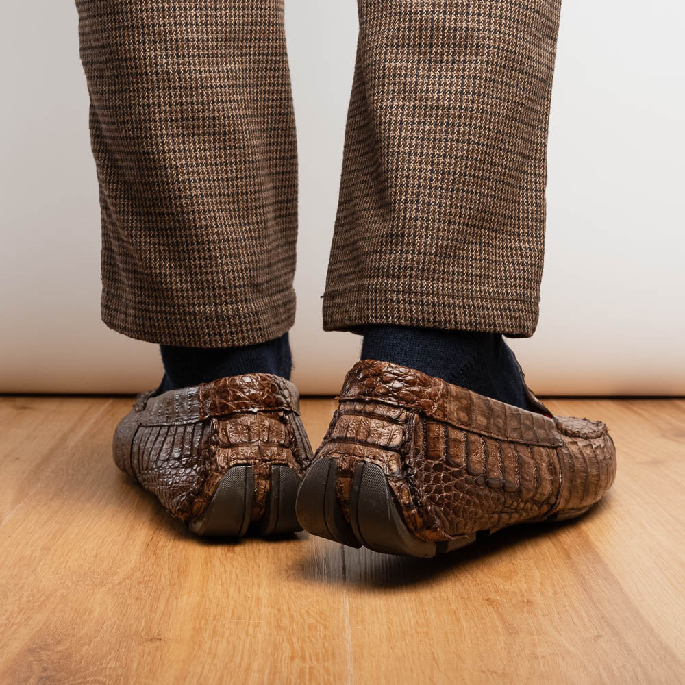 The Remo Washed Brown by Marco Di Milano features luxurious men's loafers with a crocodile texture. One shoe stands upright while the other lies on its side, revealing the detailed sole.