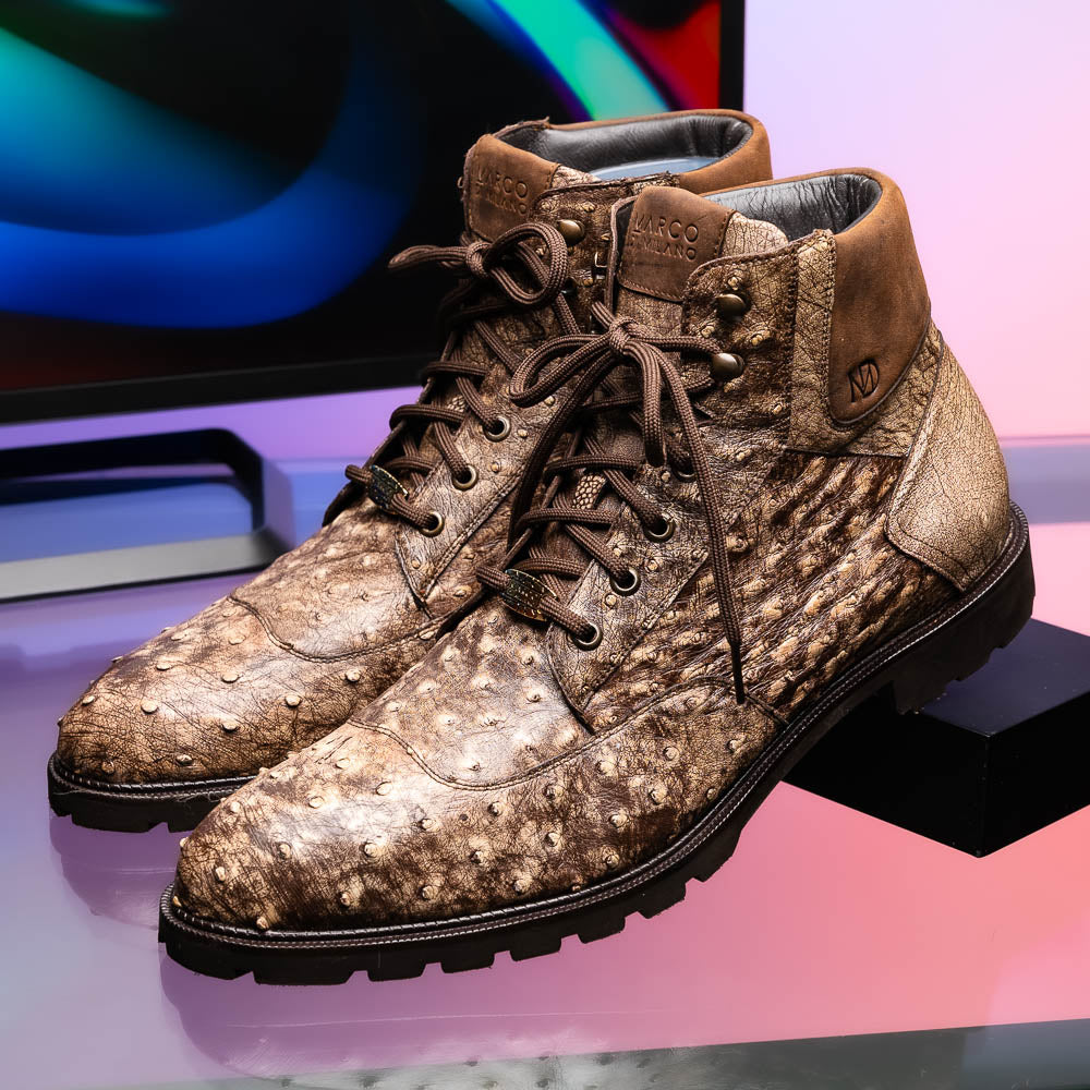 The Renzo Stone Brown by Marco Di Milano are lace-up ankle boots featuring a textured, speckled pattern and thick black rubber soles—one stands upright while the other lies on its side—ideal for luxury footwear lovers.