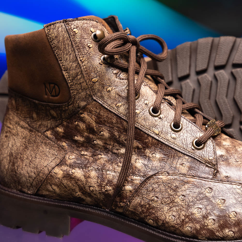 The Renzo Stone Brown by Marco Di Milano are lace-up ankle boots featuring a textured, speckled pattern and thick black rubber soles—one stands upright while the other lies on its side—ideal for luxury footwear lovers.