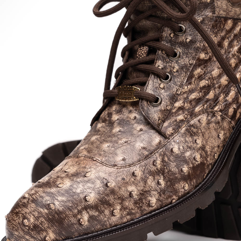 The Renzo Stone Brown by Marco Di Milano are lace-up ankle boots featuring a textured, speckled pattern and thick black rubber soles—one stands upright while the other lies on its side—ideal for luxury footwear lovers.
