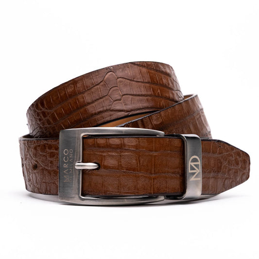 The Riccardo Belt Bay Apache by Marco Di Milano is a brown caiman belly belt with a crocodile pattern, featuring a silver buckle engraved with the brand name and "MM" initials—a true luxury exotic accessory.