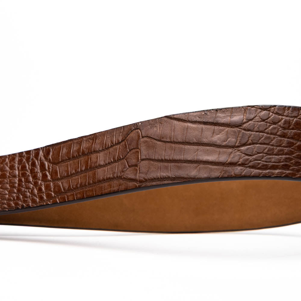 The Riccardo Belt Bay Apache by Marco Di Milano is a brown caiman belly belt with a crocodile pattern, featuring a silver buckle engraved with the brand name and "MM" initials—a true luxury exotic accessory.