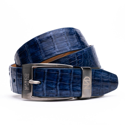 The Riccardo Belt Blue Jeans by Marco Di Milano, crafted from genuine caiman fuscus-belly leather with a crocodile-embossed finish and a silver engraved buckle, is showcased coiled on white—a bold pick for exotic belt enthusiasts.