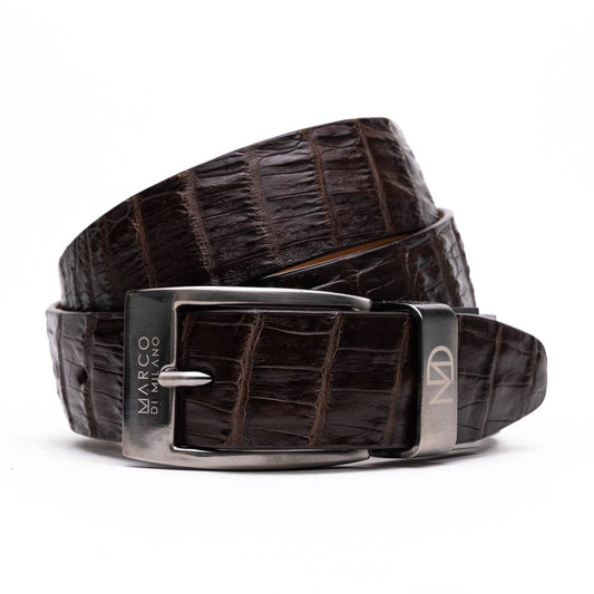 The Riccardo Belt Dark Brown by Marco Di Milano is crafted from exotic leather with a crocodile pattern and features a silver buckle engraved with the brand's name and logo.