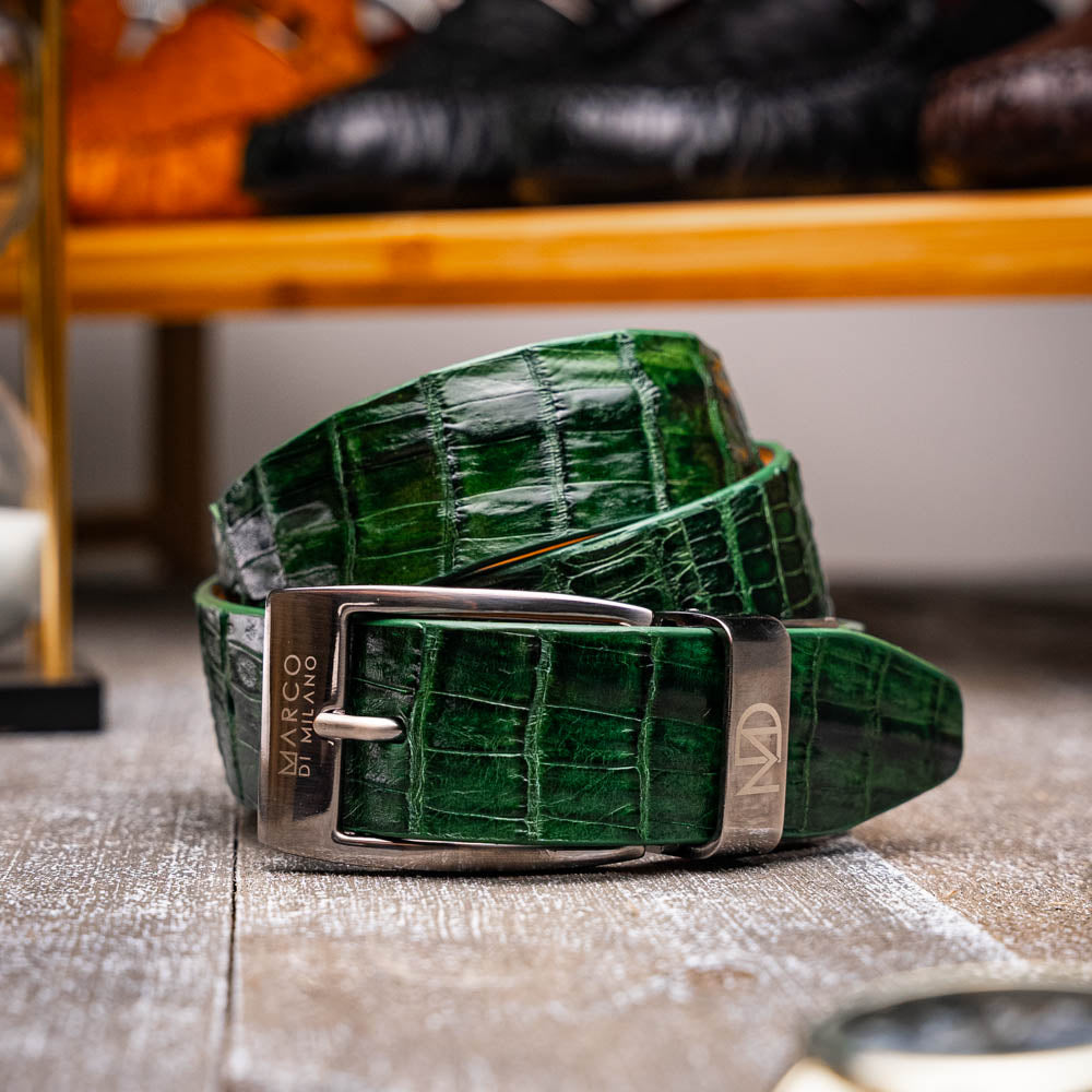 The Riccardo Belt Forest Green by Marco Di Milano features crocodile-embossed dark green leather and a silver buckle engraved with the brand logo, displayed coiled on a white background.